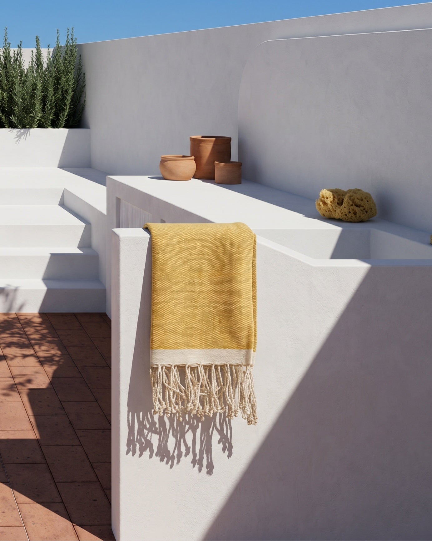 A yellow handwoven towel with cream fringe hangs from a white outdoor bathroom.
