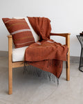 A copper-coloured cushion cover with a geometric pattern and a throw are draped over a chair.