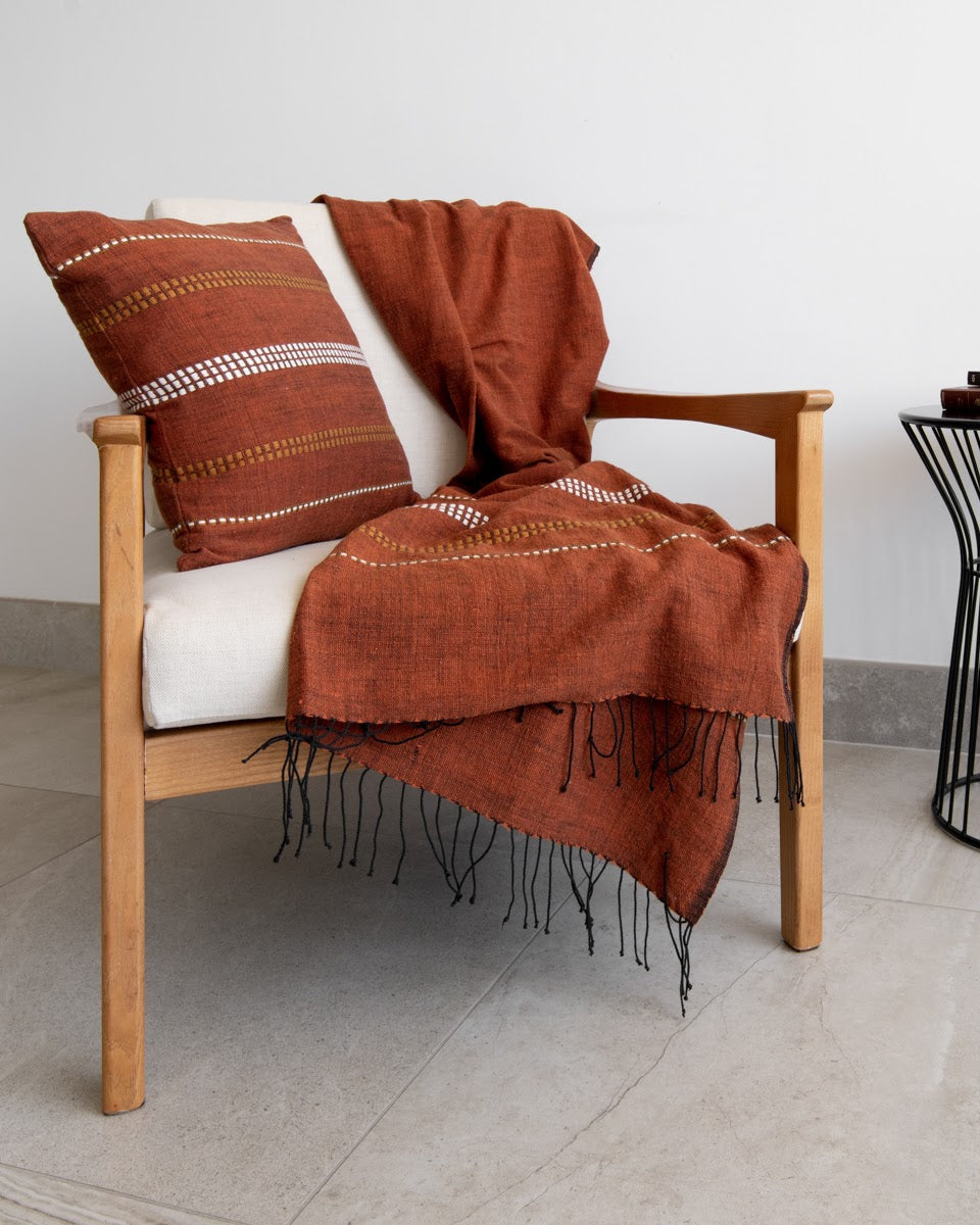 A copper-coloured cushion cover with a geometric pattern and a throw are draped over a chair.