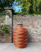 Tall terracotta geometric-patterned art basket against a brick garden wall