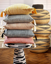 Stack of patterned cushions on a decorative stool with a woven basket in the background.