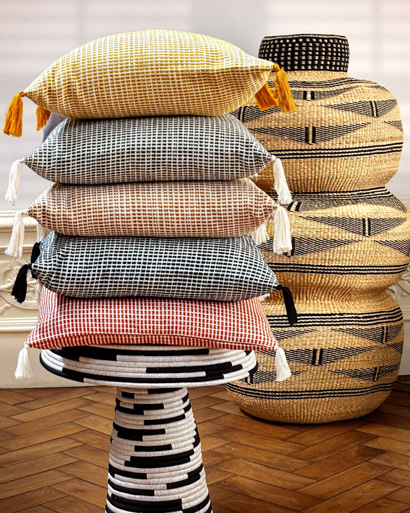 Stack of patterned cushions on a decorative stool with a woven basket in the background.
