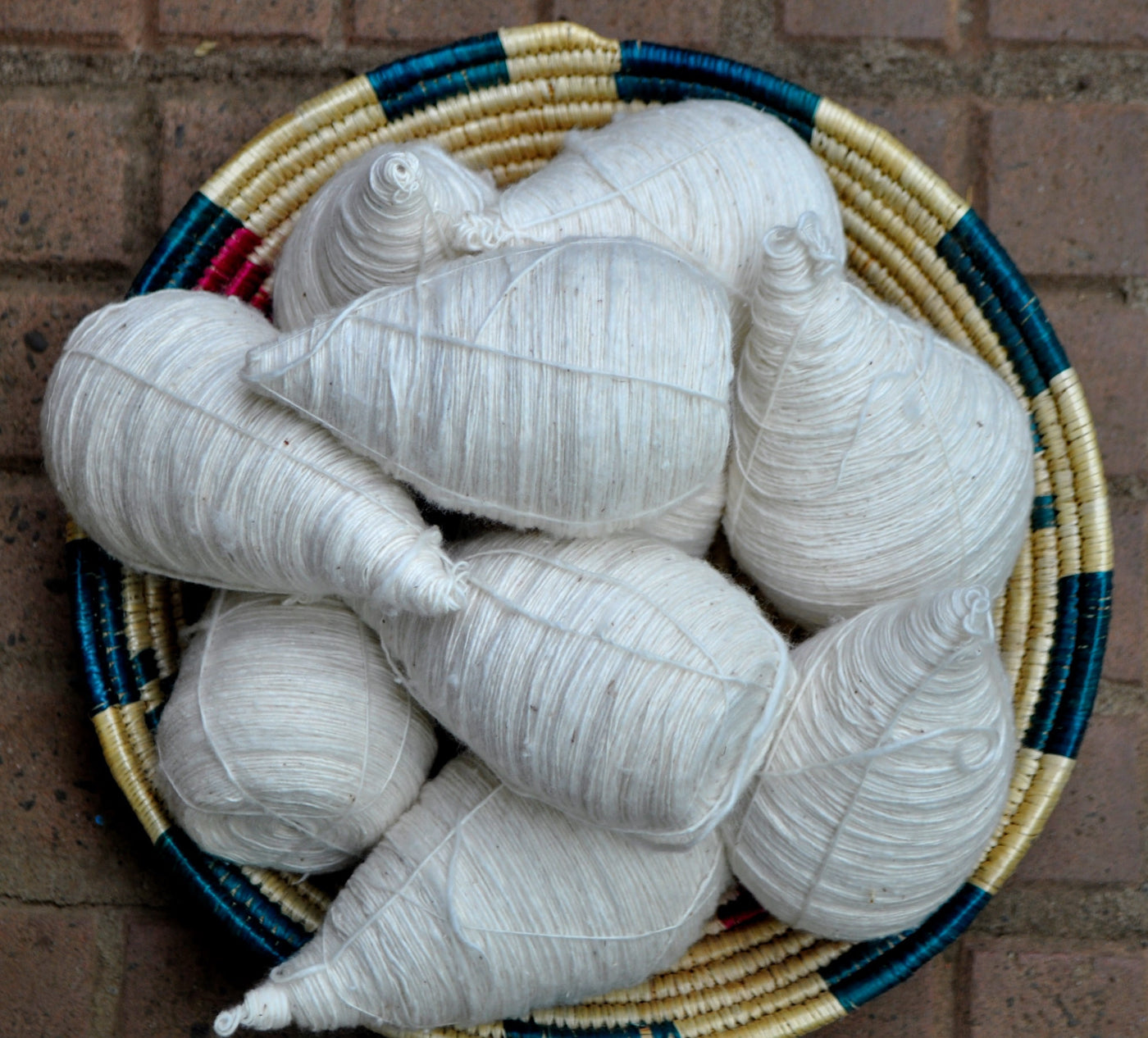 Several white thread-bobbins arranged in a round woven basket.