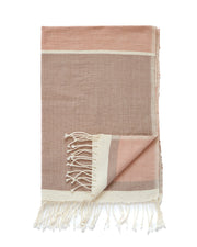 A blush coloured handwoven throw with fringes, featuring a color-blocked design in dusty pink and cream, shown on a plain white background.
