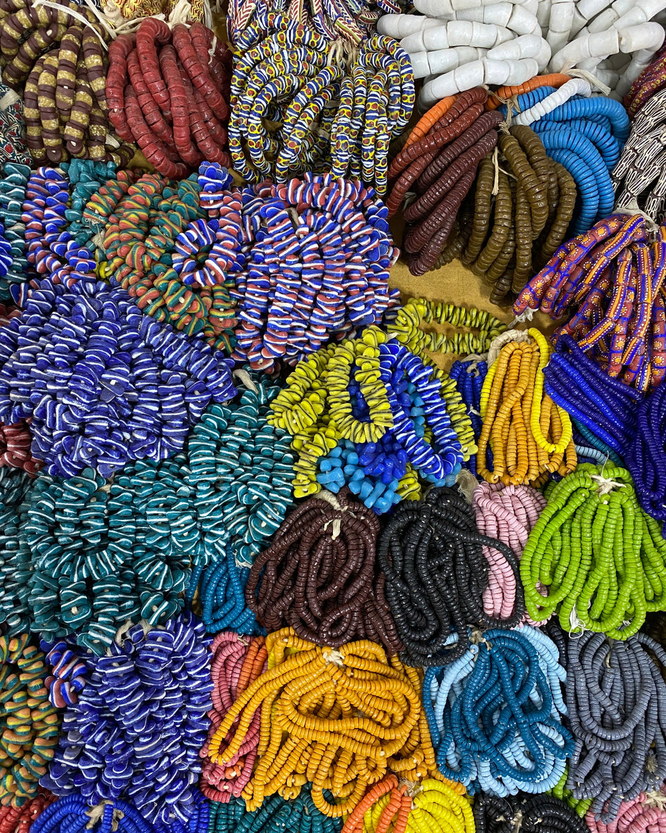 A dense, colorful display of coiled beaded bracelets or necklaces made of small round beads, arranged in overlapping bundles of blue, purple, yellow, green, pink, brown, black, and white.