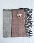 A hand woven small towel with dark fringes, laid flat on a white background. The left side is gray, the center-right is dusty mauve pink, and there is a thin dark vertical stripe between them.