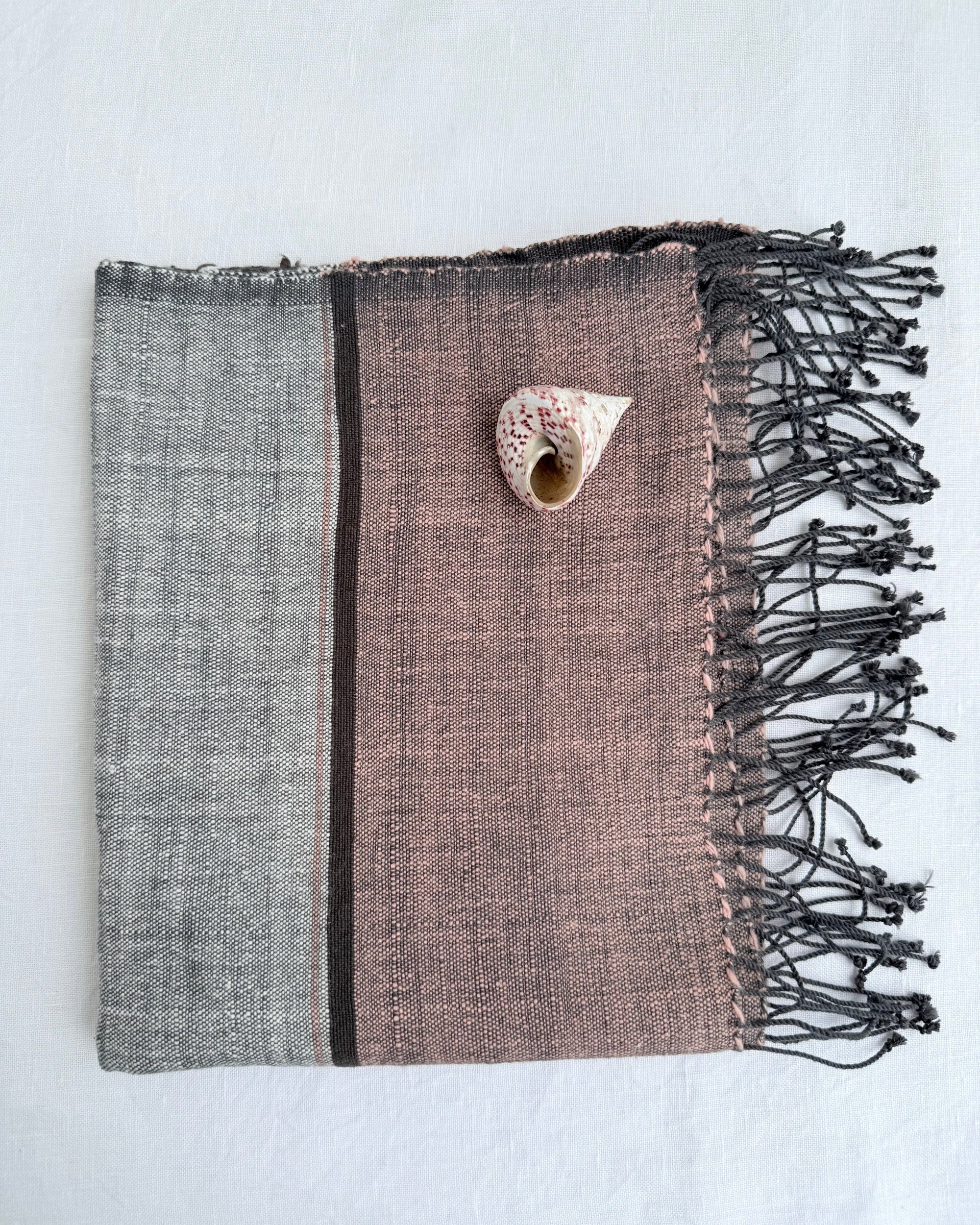 A hand woven small towel with dark fringes, laid flat on a white background. The left side is gray, the center-right is dusty mauve pink, and there is a thin dark vertical stripe between them.