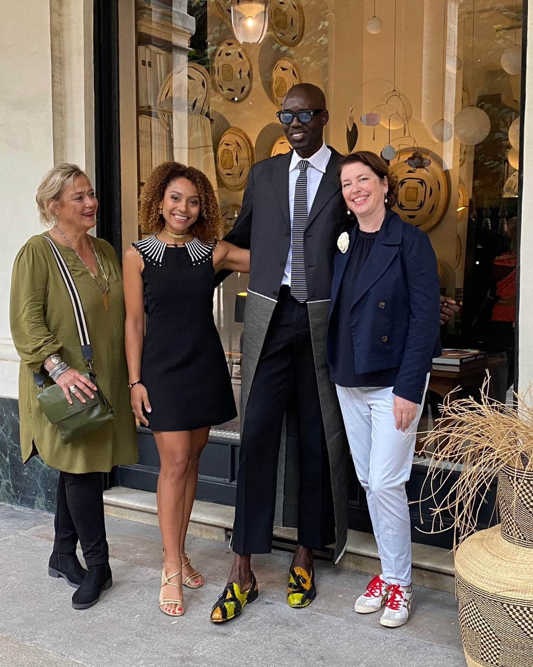 Four people posing in front of a boutique storefront. The group includes a man in a black suit and sunglasses and a woman in a navy blazer and white pants.