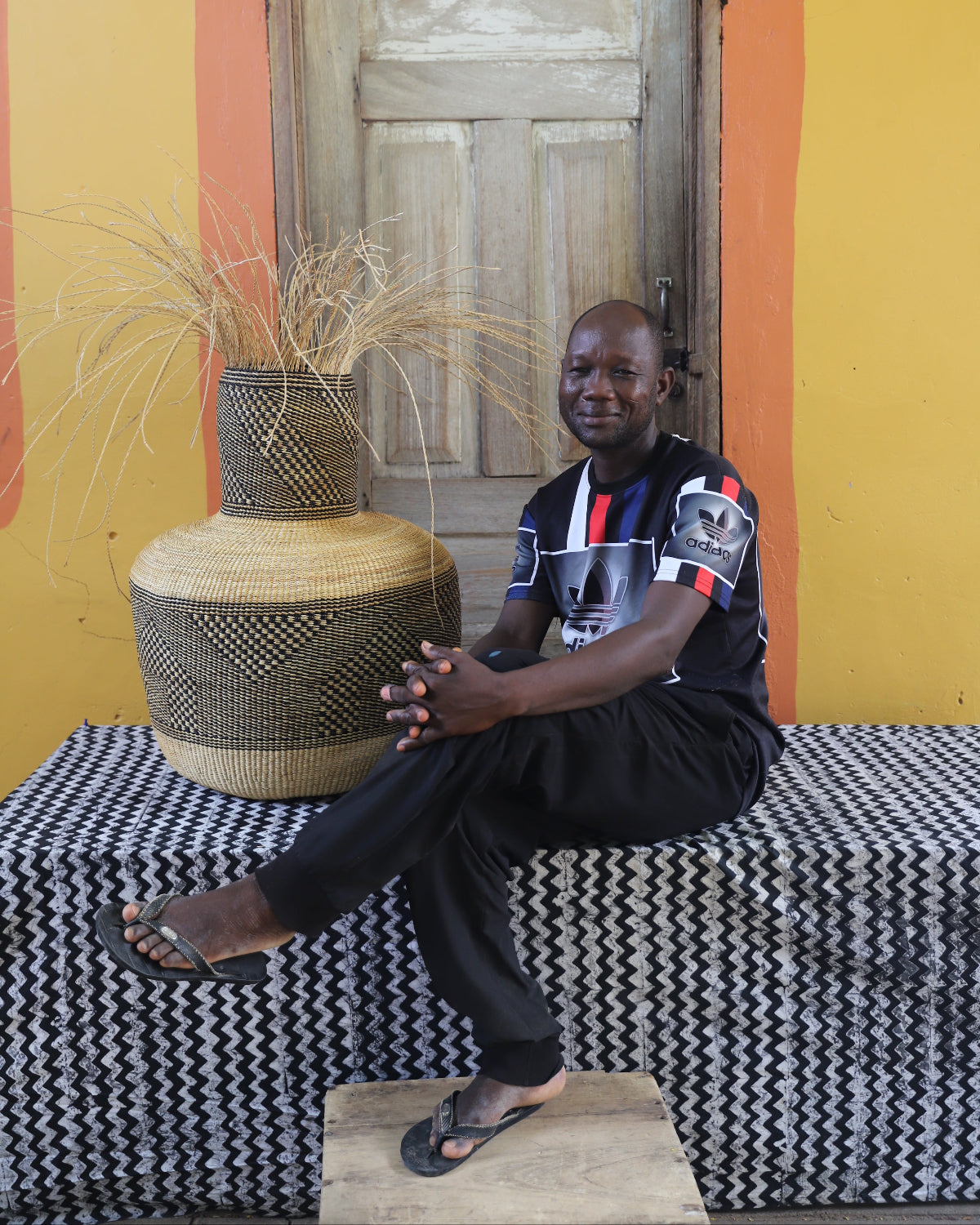 A person sitting on a bench beside a large, decorative art basket with a geometric pattern.