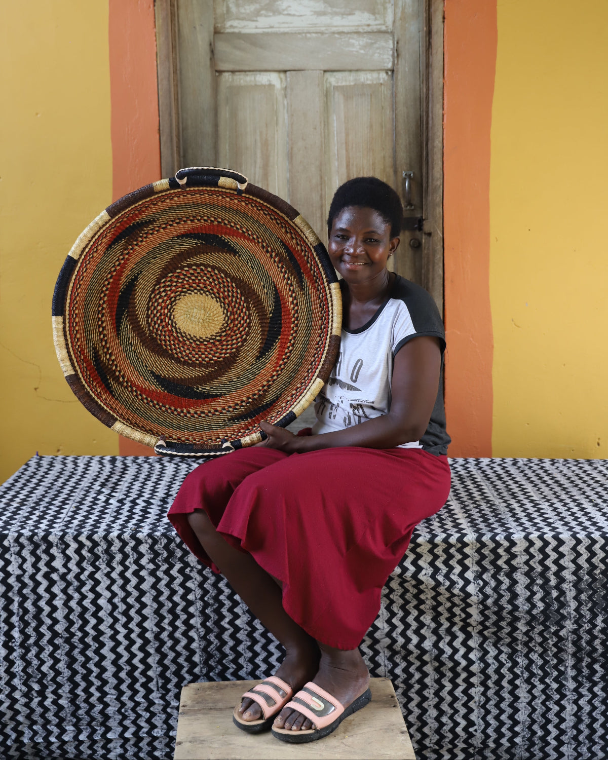 A person sitting on a bench with a wall hanging double weave basketry art behind them, displaying a patterned design.