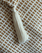 Close-up of a woven textile with a repeating brown and off-white check pattern and a cream tassel tie at the top.