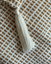 Close-up of a woven textile with a repeating brown and off-white check pattern and a cream tassel tie at the top.