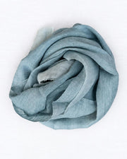 A light blue-gray silk scarf, elegantly draped and rolled into a spiral shape against a clean white background.