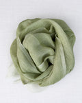 A light sage green scarf, draped and folded into a loose rosette shape, displayed on a clean white textured fabric background.