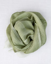 A light sage green scarf, draped and folded into a loose rosette shape, displayed on a clean white textured fabric background.