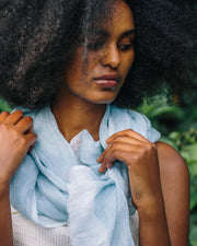 Woman wearing a light blue scarf against a green leafy background