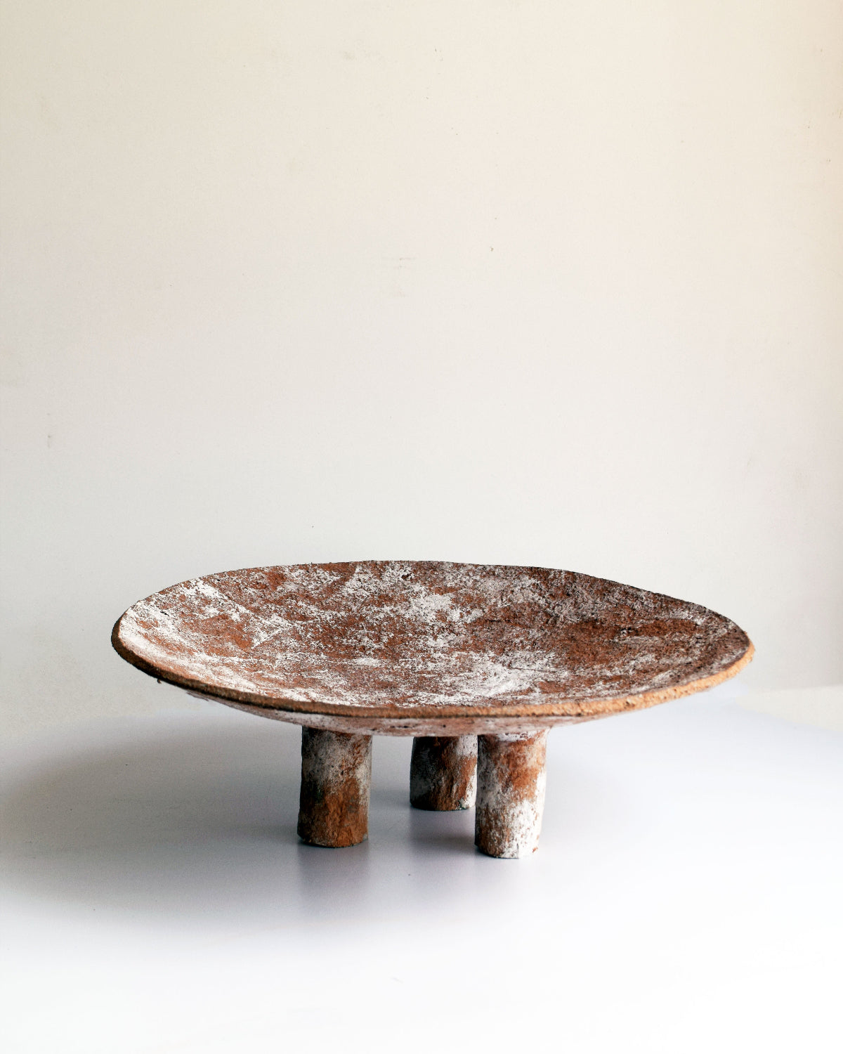 A terracotta coloured paper pulp Swazi platter with a white texture, featuring a round shape with three legs.