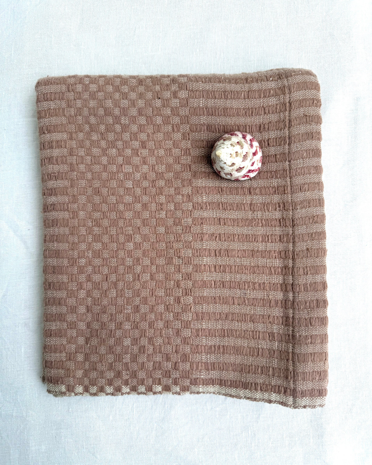 A blush colored cotton hand towel, laid flat on a white fabric background.