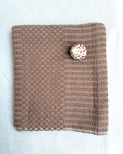A blush colored cotton hand towel, laid flat on a white fabric background.