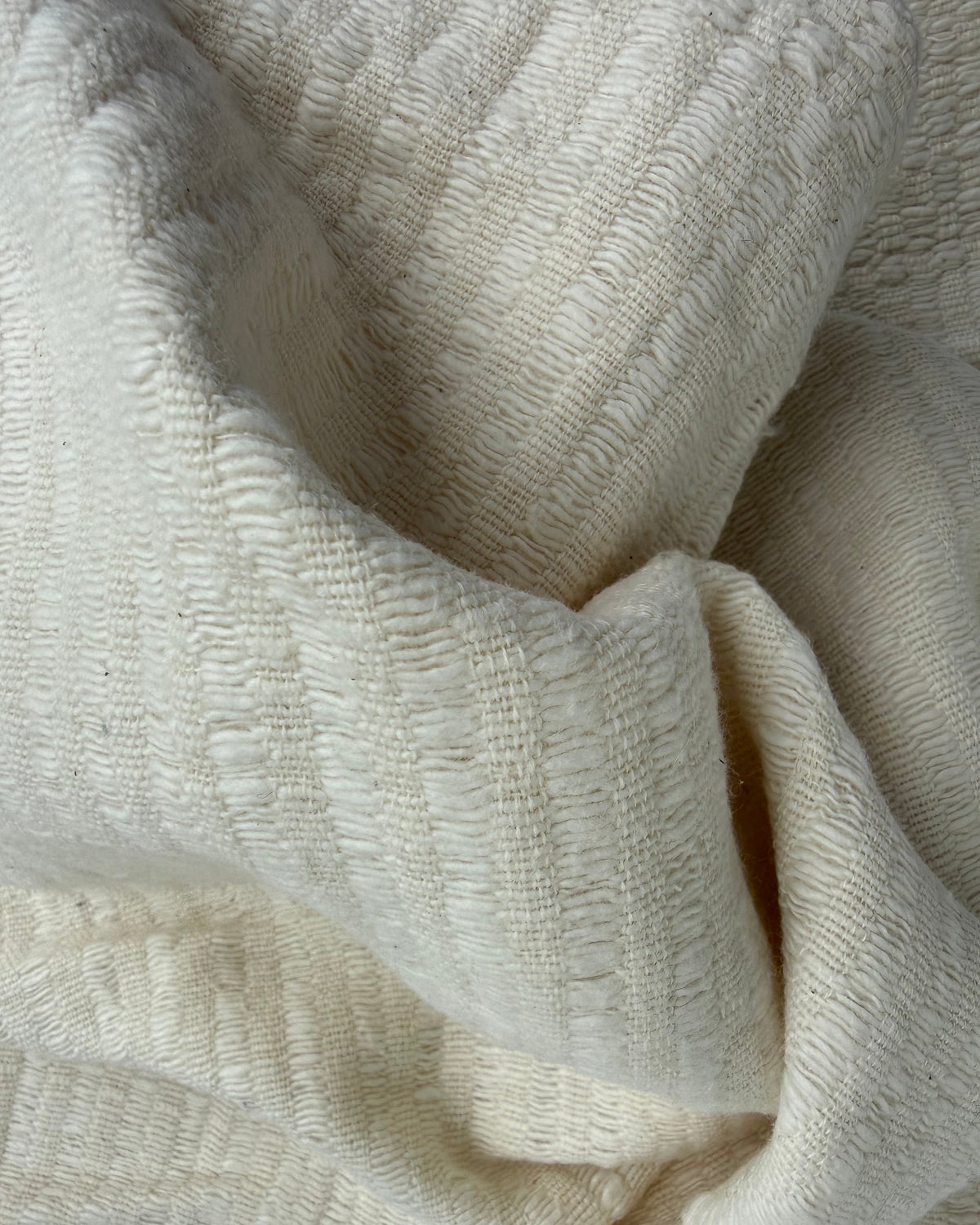 A close-up of draped cream-colored textured fabric with a ribbed, woven pattern.