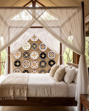 A luxury four-poster canopy bed with white drapes, set in a rustic cabin with a decorative wall art made from basketry.
