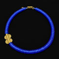 A vibrant cobalt blue beaded necklace with a textured spiral pattern and gold-toned metal accents, displayed on a solid black background.