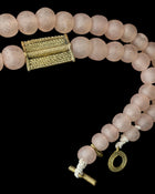 Rose quartz bead mala necklace with a textured gold clasp and toggle, shown against a solid black background.