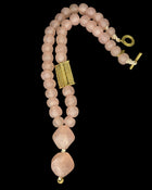 A rose quartz beaded necklace with a textured gold rectangular centerpiece and a toggle clasp, displayed on a solid black background.