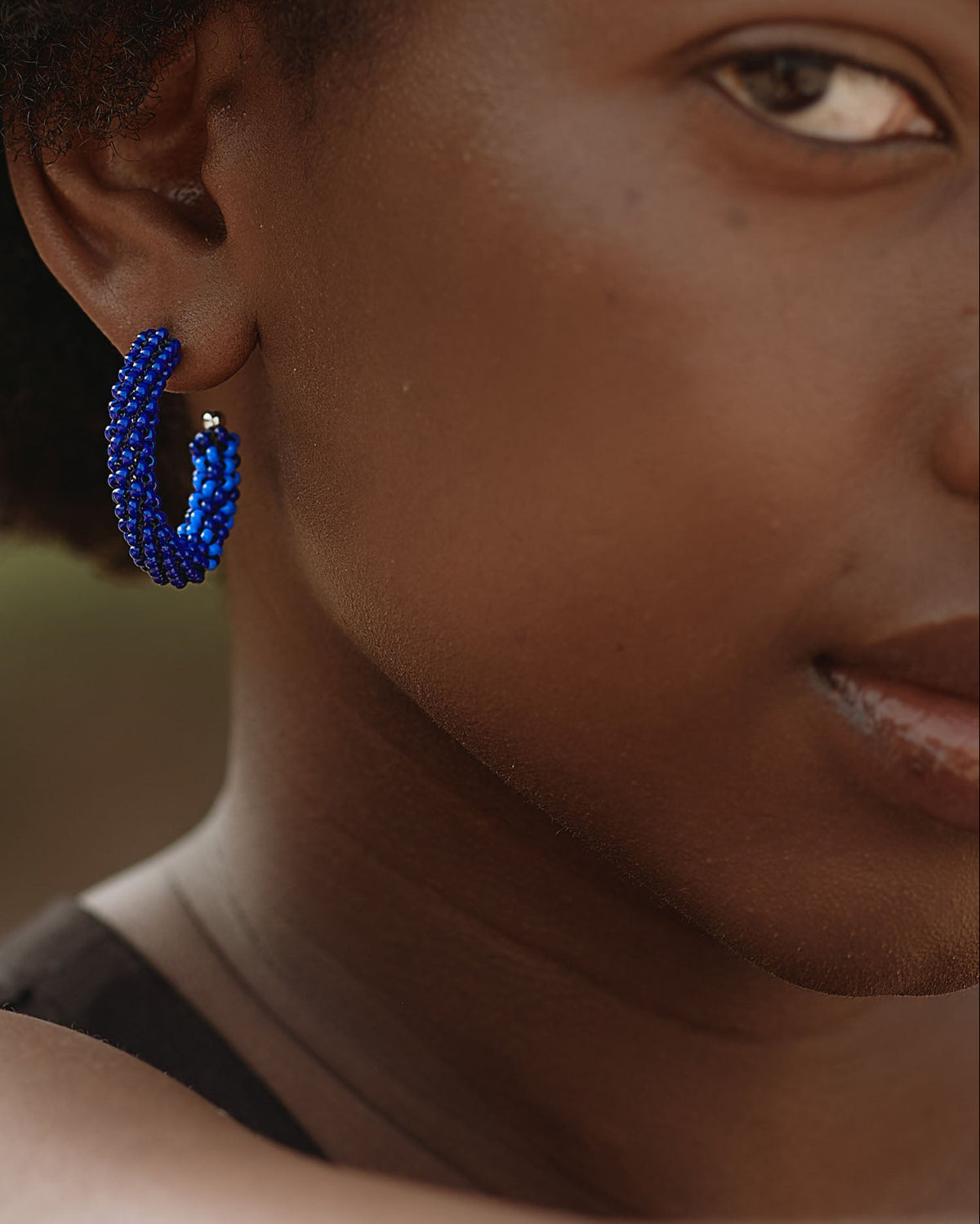 A person wearing blue hoop earrings with silver-plated findings.