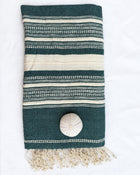 A folded dark green and cream striped woven throw blanket with fringe tassels and a round decorative accent, laid flat on a white background.