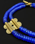 A close-up of a double-strand beaded necklace featuring vibrant blue faceted beads and textured gold-toned spiral accents, displayed on a solid black background.