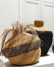 A collection of hand-woven art baskets vases and decorative pots displayed on a white gallery shelf against a white paneled wall, with a framed Samburu portrait hanging in the background.