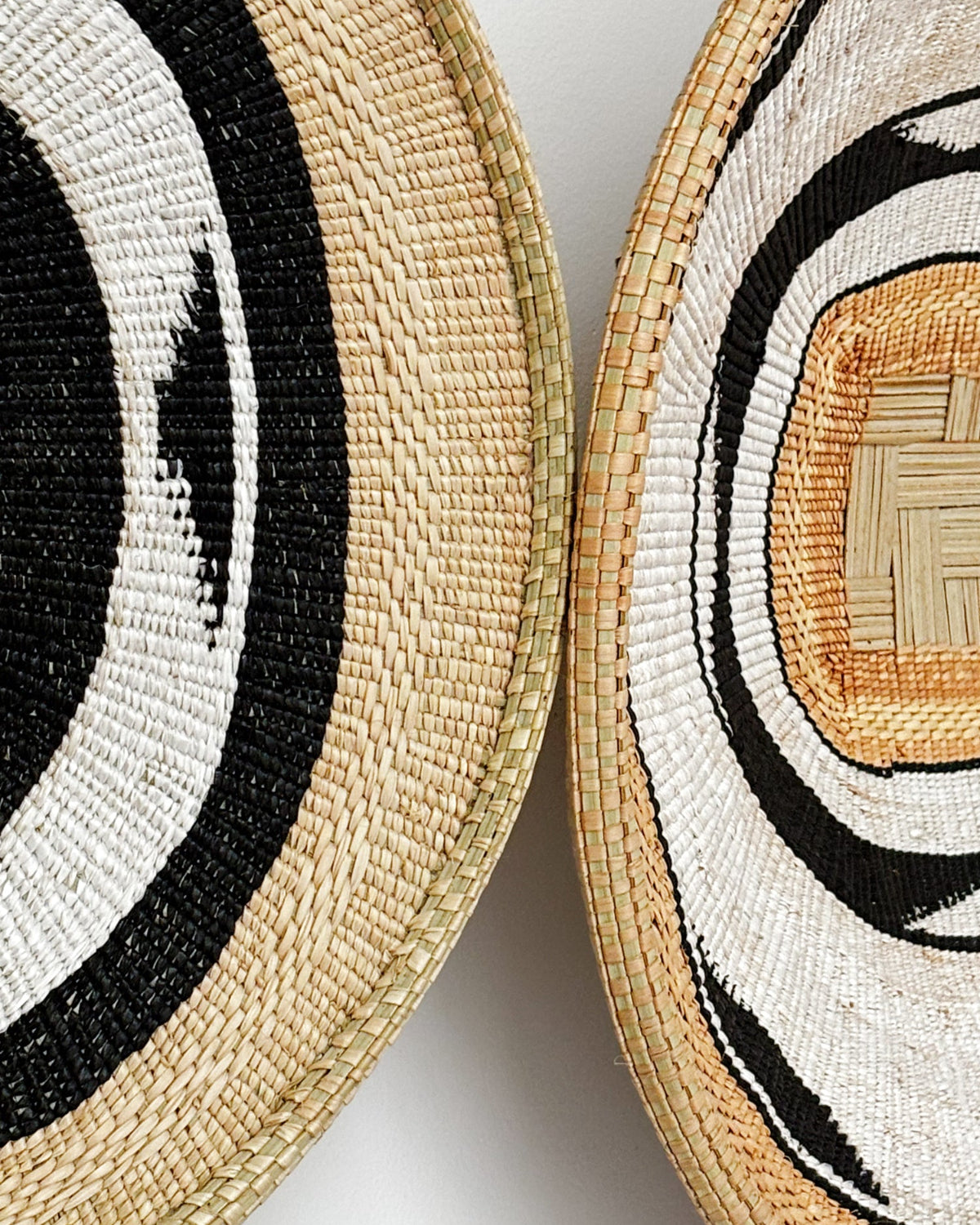 Two woven round baskets shown in a close-up detail shot, featuring natural straw tones with black and white concentric circular patterns.