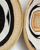 Two woven round baskets shown in a close-up detail shot, featuring natural straw tones with black and white concentric circular patterns.