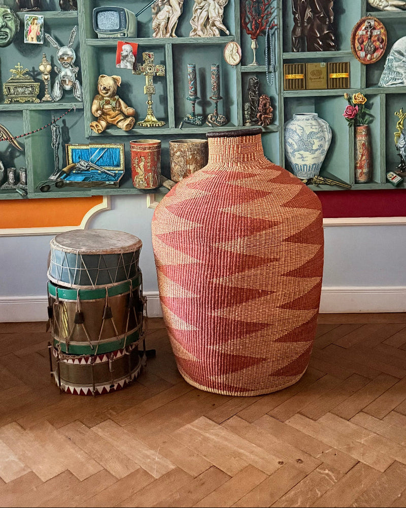 Terracotta art basket beside a drum in a room with shelves of objects